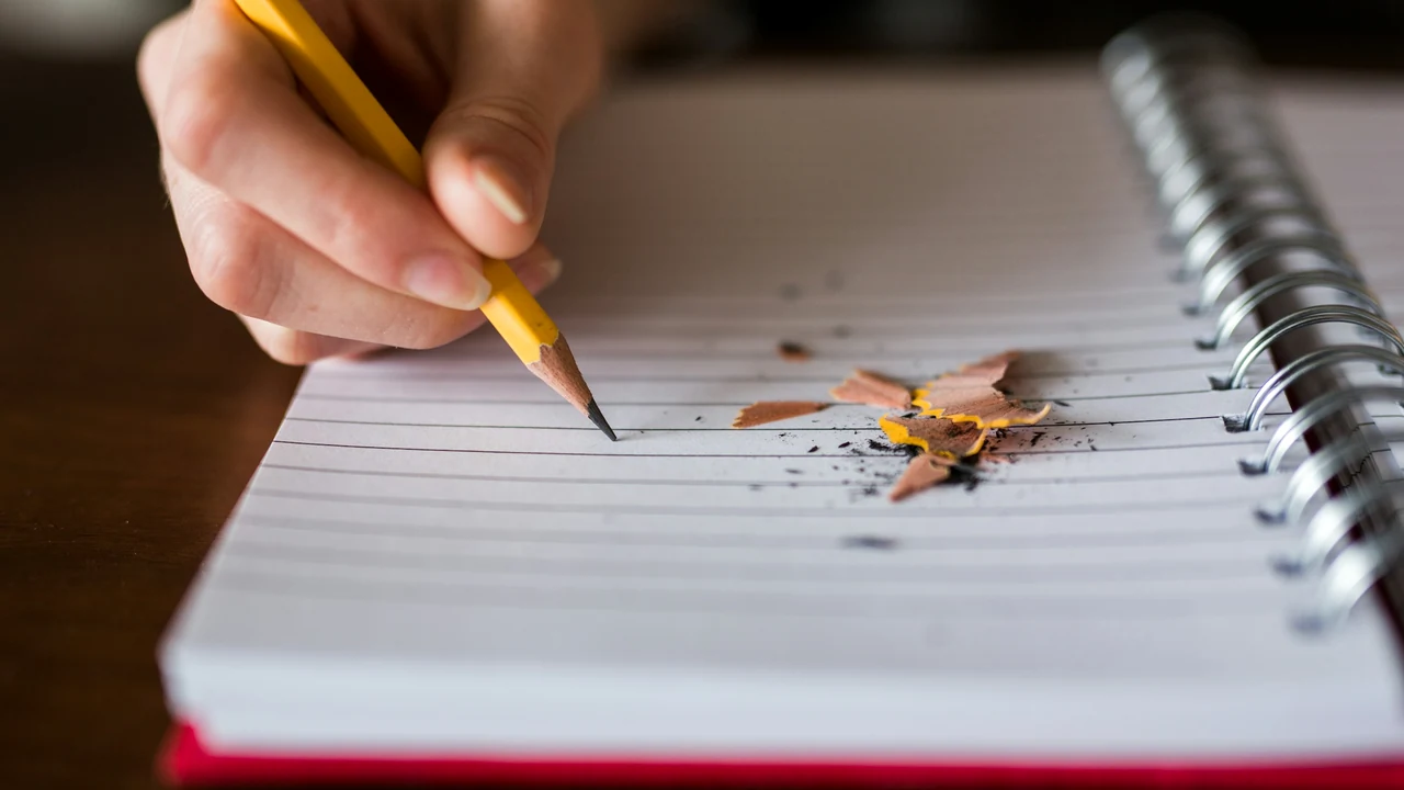 Hand taking careful notes with a pencil on a blank page.