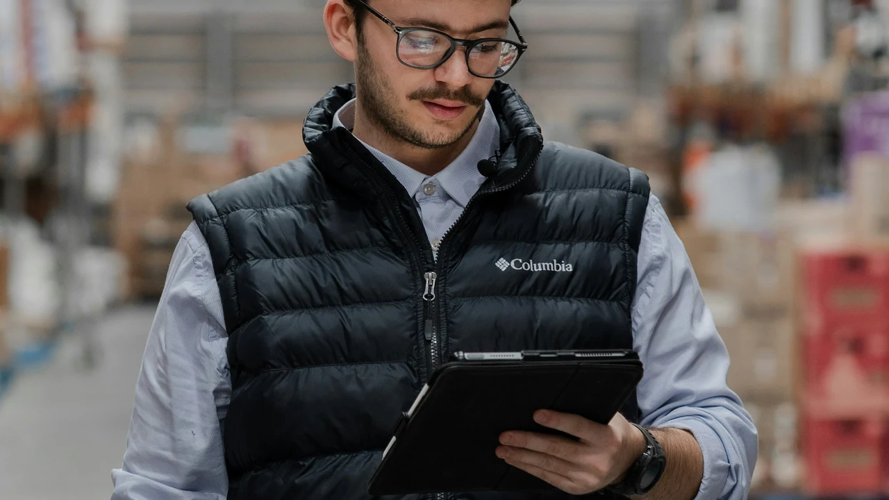 Authentic photograph of man in vest using tablet in a warehouse.