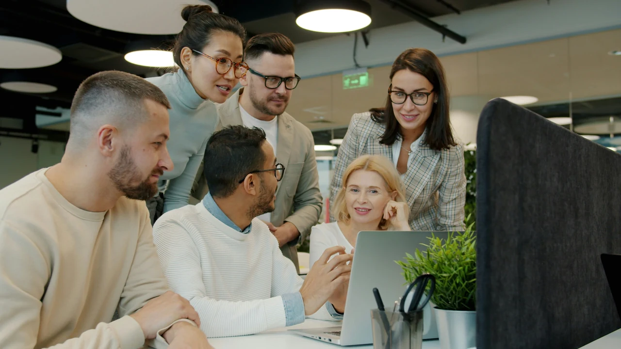 Authentic photograph of diverse team collaborating around a laptop in office.