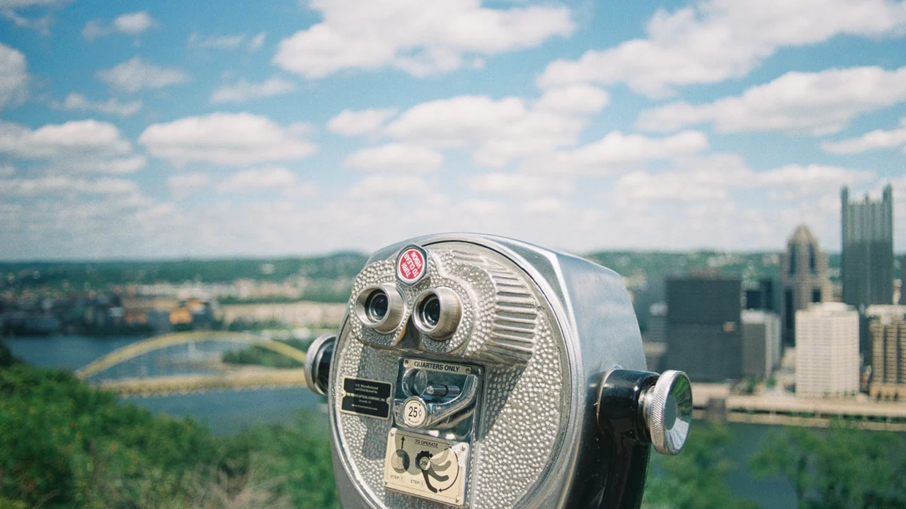 Public viewing binoculars overlooking a broad city landscape.