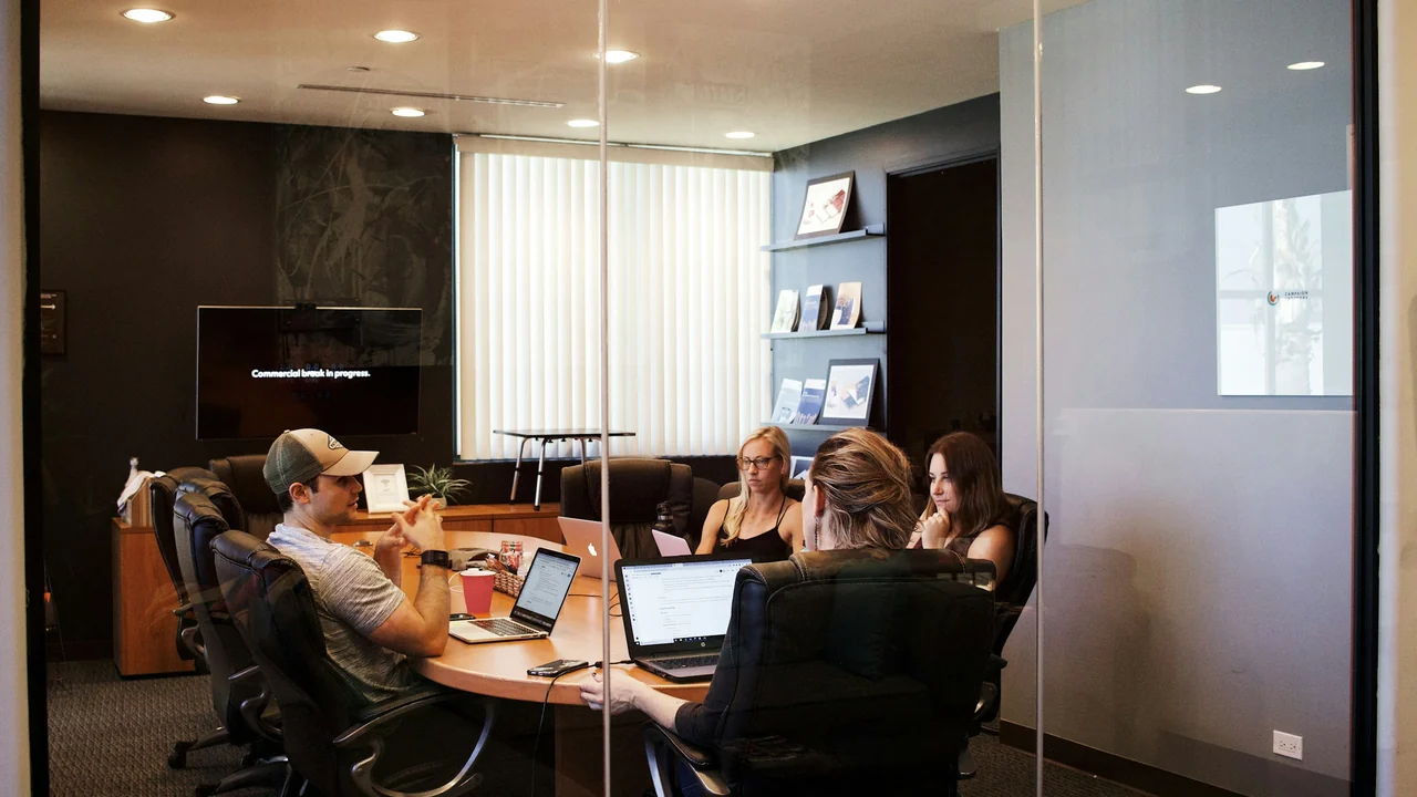 Marketing collaborators working around a conference table with laptops and planning materials.