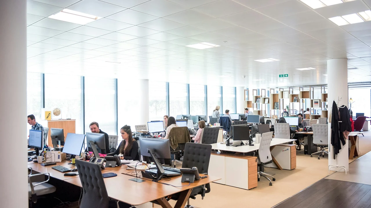 People working at connected desks in a bright open office.