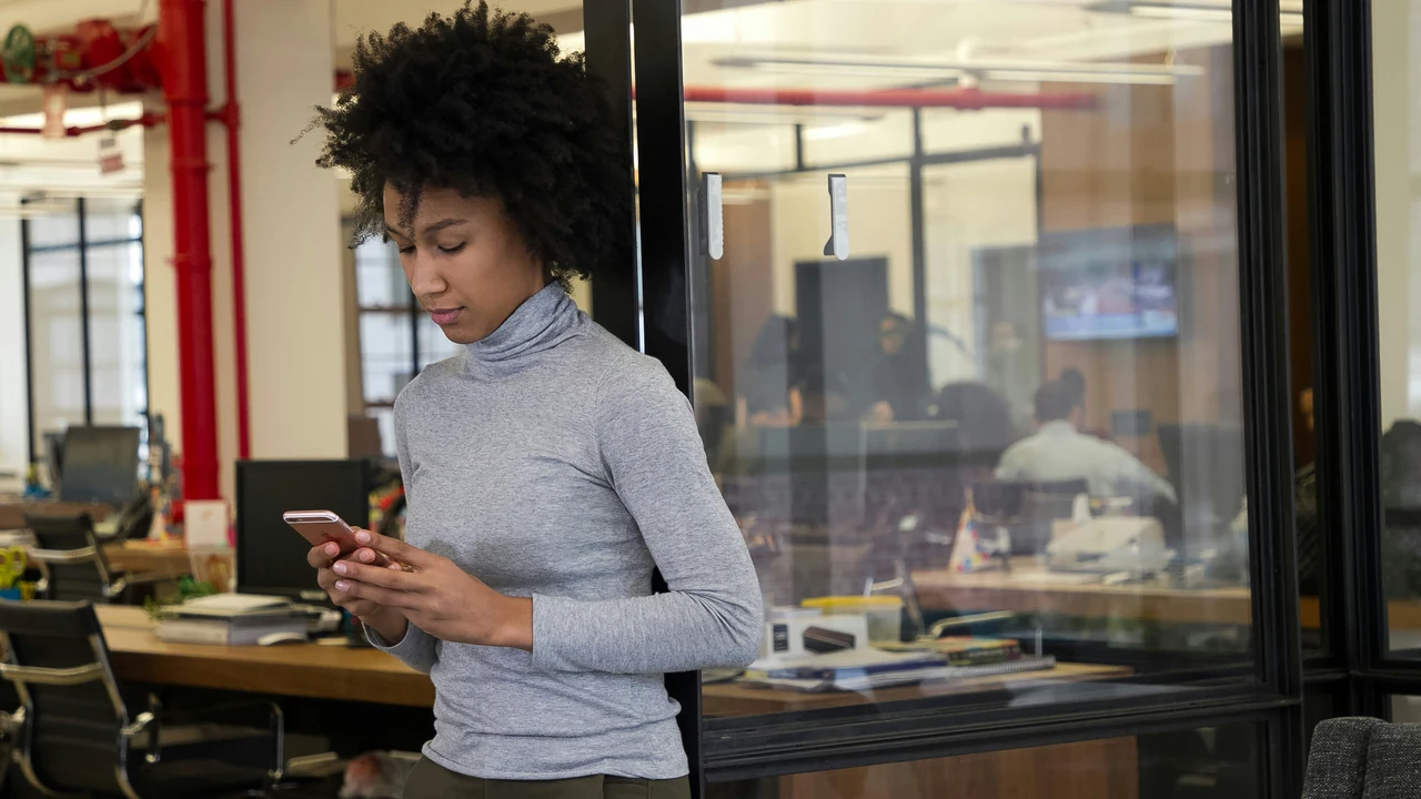 A woman standing in an office looking at her cell phone.