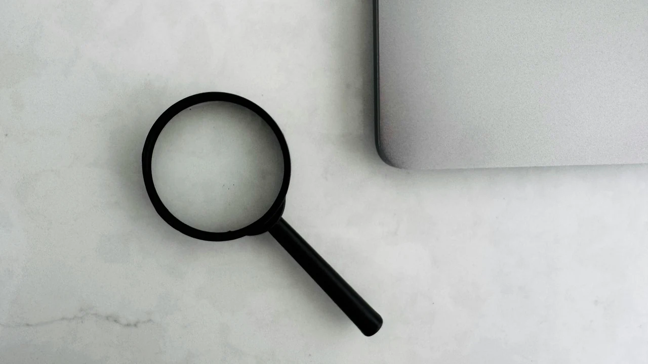 Magnifying glass beside a laptop during online search research.