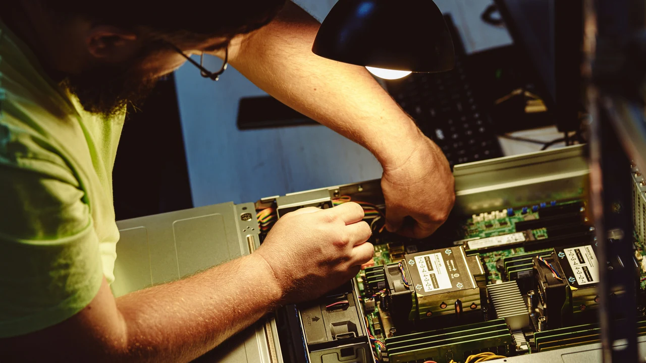 Technician repairing computer server equipment under a work light.