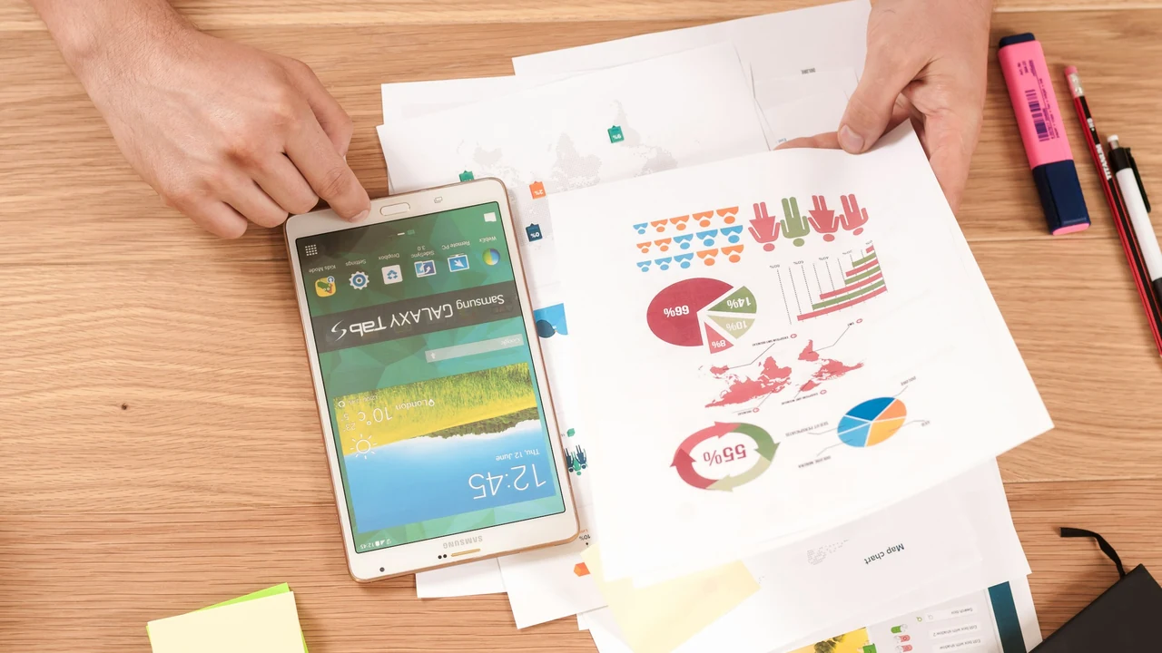 Hands reviewing printed charts and reports around a tablet.